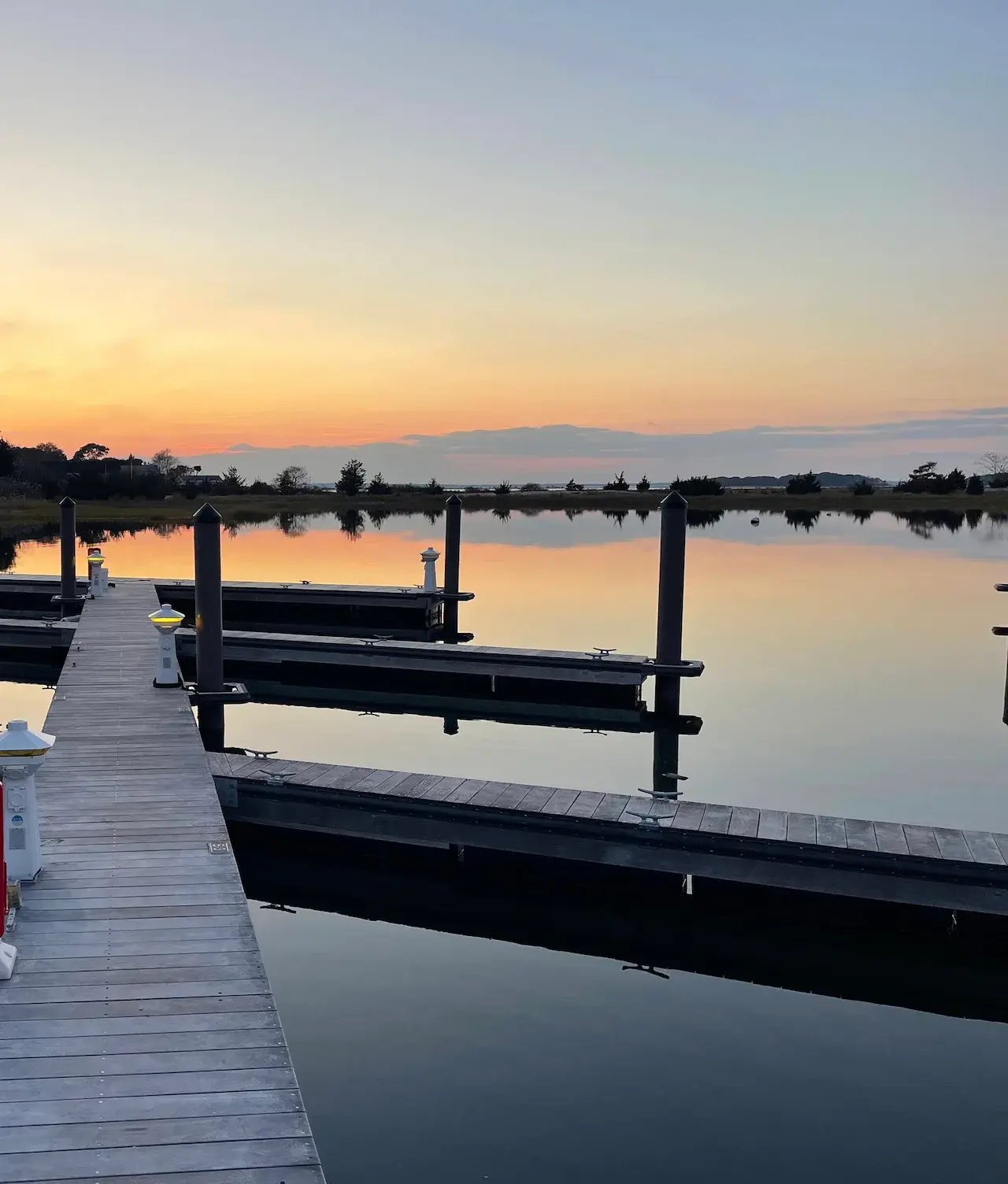 Empty marina docks reflect in calm water beneath a soft orange and blue sunset.